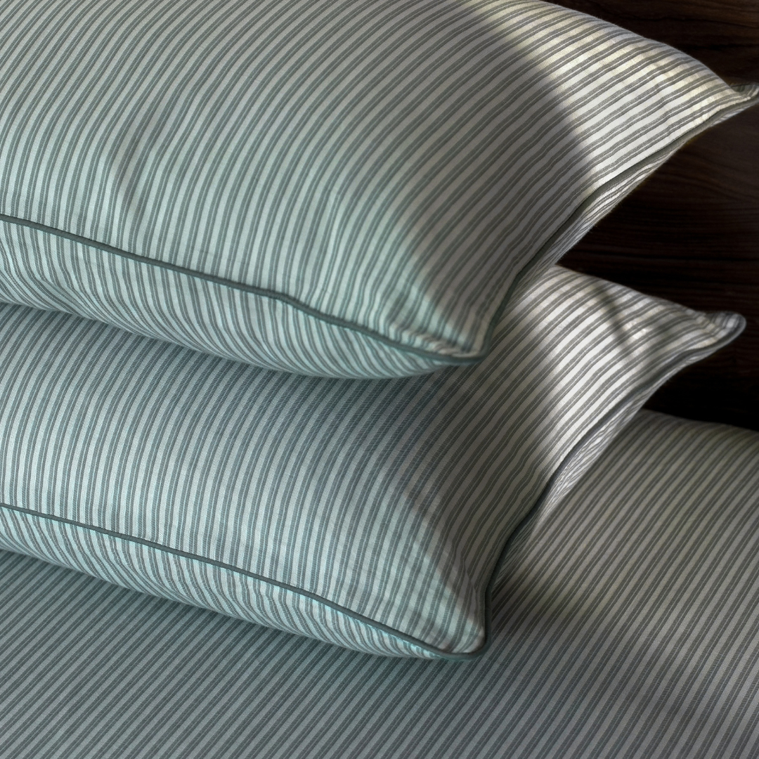 Two pine green pin stripe pillow covers stacked, showing the contrast piped edge