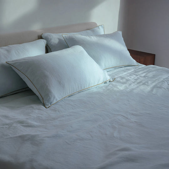 Light blue bedding set with pillows on a bed in a softly lit room.
